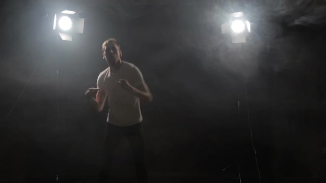 a guy in a white poppy dancing. a man rhythmically moving in the spotlight