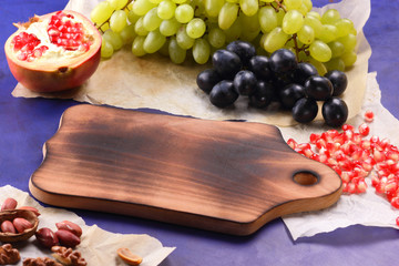 Dark blue grapes, red pomegranate, green grapes, peanuts and walnut on a wooden board with an empty place for writing in retro style