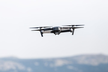 A beautiful modern black drone quadrocopter with the photo and a video camera on the board flies against the blue sky