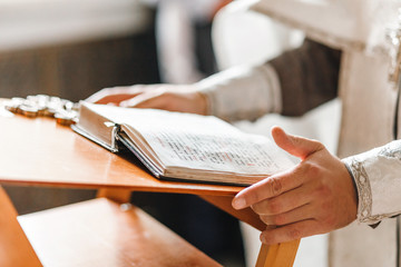 Priest hands close up on the opened bible book, during church service