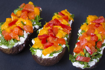 Baked eggplants stuffed with vegetable and cheese on a black slate background, close up