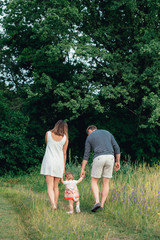 Obraz premium young happy family with little beautiful baby with blue eyes walking in summer park at sunset.