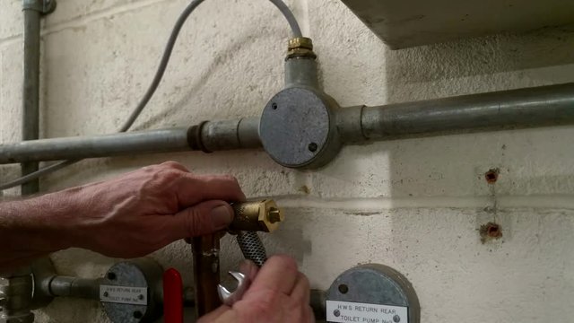 Plumber opening a drain valve on heating pipework with a spanner