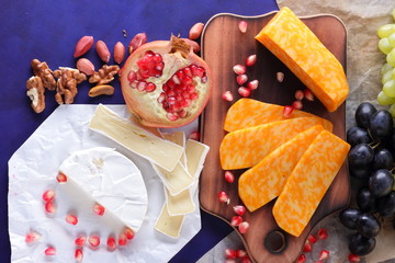 Camembert cheese, marbled cheese, different cheeses, dark blue grapes, red pomegranate, green grapes, peanuts and walnuts on a wooden board with an empty place for writing in retro style