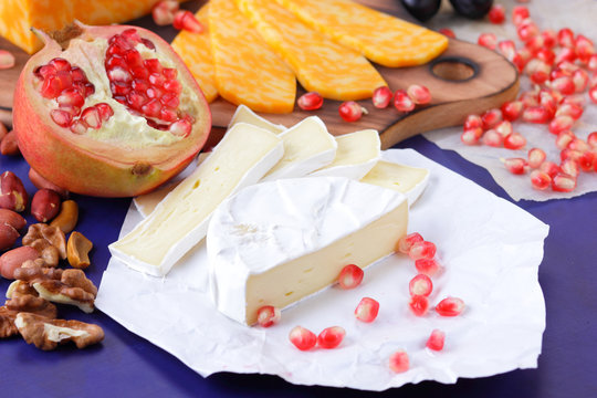Camembert cheese, marbled cheese, different cheeses, dark blue grapes, red pomegranate, green grapes, peanuts and walnuts on a wooden board with an empty place for writing in retro style