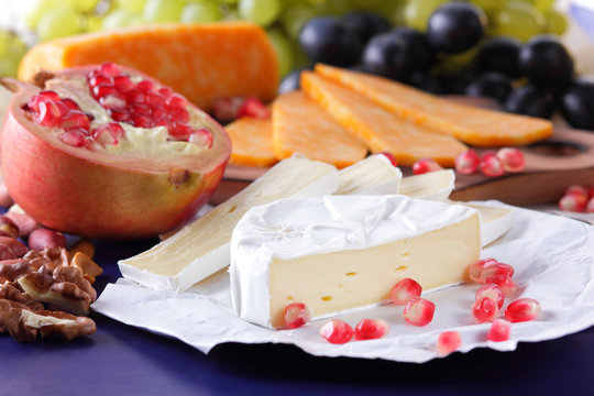 Camembert cheese, marbled cheese, different cheeses, dark blue grapes, red pomegranate, green grapes, peanuts and walnuts on a wooden board with an empty place for writing in retro style