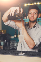 Young bartender pouring cocktail drink into glass