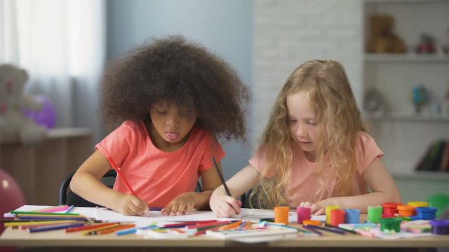 Young multiracial females sitting at the table and drawing with colorful pencils