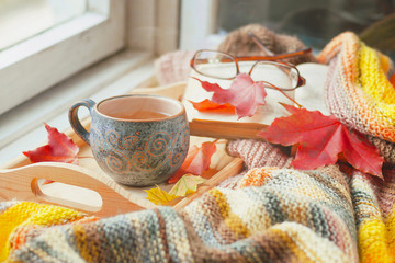 A сup of hot tea, a book and maple leaves on the wooden windowsill. Autumn concept.