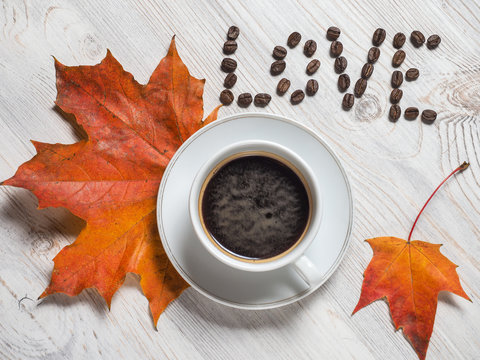 Autumn, autumn leaf of maple with a hot Cup of coffee and an inscription of the coffee bean love on the background of wooden table. Seasonal, morning coffee, Sunday rest and the concept of still life.