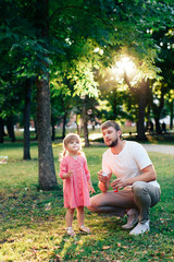 Fototapeta premium happy father with a small daughter at sunset blowing soap bubbles in a summer park outdoors