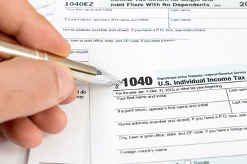 Male hand holding pen and pointing on tax form 1040. Business concept.