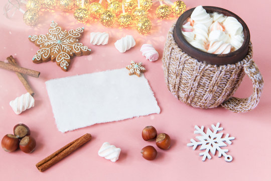 Christmas greeting card, hot chocolate with marshmallow, cinnamon, snowflake on light pink table. Top view with copy space