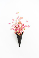 Black ice cream waffle cone with dry pink roses petals isolated on white background. Flat lay, top view flower concept.