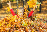Happy little girl plays with autumn leaves in the park