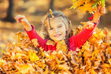 Happy little girl plays with autumn leaves in the park