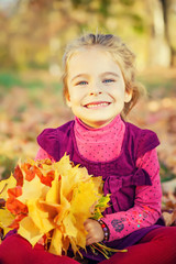 Happy little girl with autumn leaves in the park