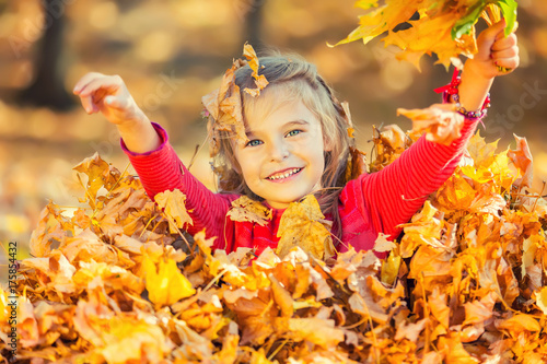 Happy little girl plays with autumn leaves in the park