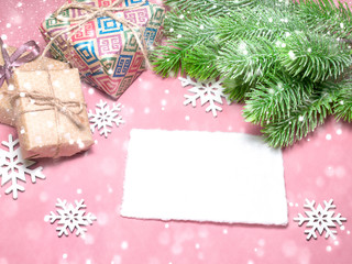 Christmas greeting card over light pink table with snowflakes, gifts, fir tree branches. Flat lay style