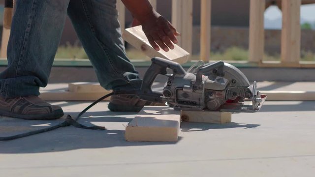 Worker Cuts Wood Partial Using Foot as Leverage. a construction worker quickly cuts wood using his foot as leverage. 
