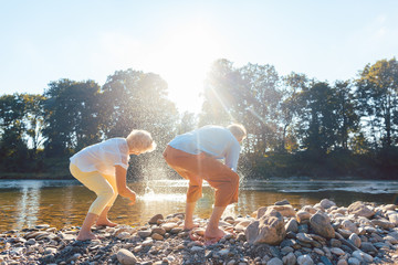 Two senior people enjoying retirement and simplicity while throwing stones into the river - obrazy, fototapety, plakaty