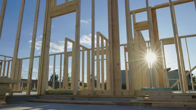 Move Left Through a Construction Site of a Framed Home. view moves left as sun flare wraps around the beams of the new residential home framing wood walls
