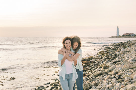 Mom and her teenage daughter hugging and smiling together over sunset sea view.Beautiful woman relaxing with her child.