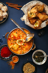 Indian cuisine on diwali holiday: tikka masala, samosa, patties and sweets with mint chutney and spices. Dark blue background. Vertical composition