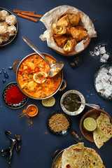 Indian cuisine on diwali holiday: tikka masala, samosa, patties and sweets with mint chutney and spices. Dark blue background. Vertical composition