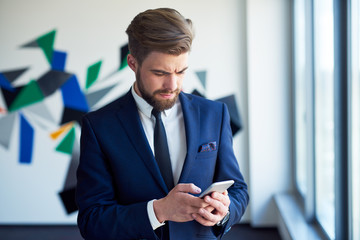 Worried businessman checking phone in office, receiving bad news