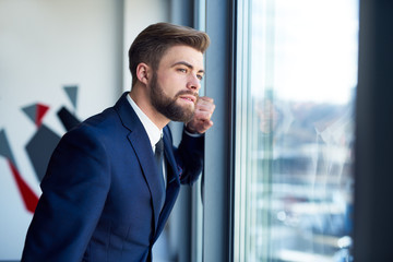 Young businessman looking through the window in office