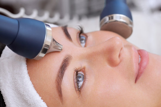 The cosmetologist makes the procedure an ultrasonic cleaning of the facial skin of a beautiful, young woman in a beauty salon.Cosmetology and professional skin care.