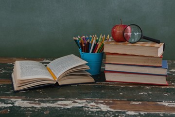 Stack of books with apple, magnifying glass and pen holder