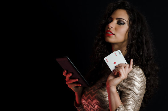 Sexy curly hair brunette posing with tablet and aces in her hands, online poker concept black background