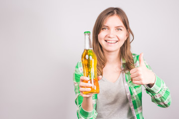Young woman holding bottle of beer and showing thumbs up gesture