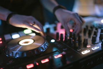 Fototapeta na wymiar Hands of woman DJ tweak various track controls on dj's deck at night club 