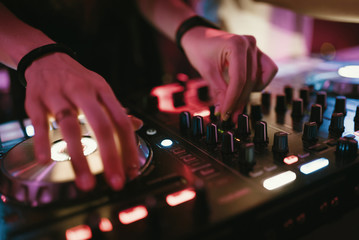Hands of woman DJ tweak various track controls on dj's deck at night club 