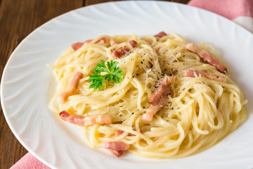 Classic pasta carbonara. Spaghetti with bacon, egg yolk and parmesan cheese on white plate on dark wooden background.