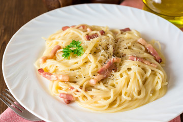 Classic pasta carbonara. Spaghetti with bacon, egg yolk and parmesan cheese on white plate on dark wooden background.