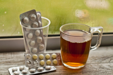 medicines, medicine and tablets in blasters and tea in a cup by the window. Autumn rain. Concept of health