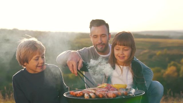 Father with children cook sausages on grill.