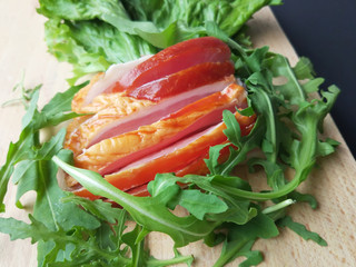 Sliced ham with fresh green lettuce leaves on a cutting board.