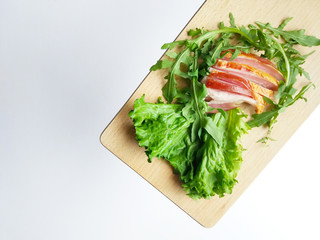 Sliced ham with fresh green lettuce leaves on a cutting board.