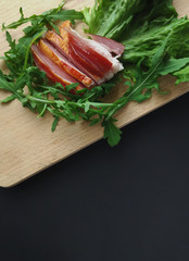Sliced ham with fresh green lettuce leaves on a cutting board.