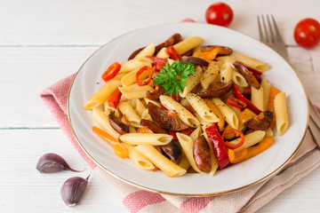 Penne pasta with mushrooms, bell pepper, chilli and parsley on white plate on white wooden background.