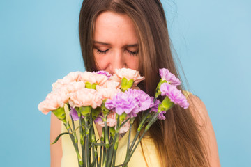 Portrait of beautiful young woman holding a bouquet of carnation flowers on a blue background, feminine, celebration