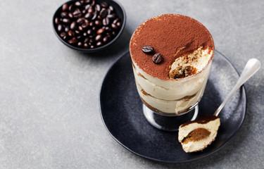 Tiramisu, traditional Italian dessert in glass on a grey stone background