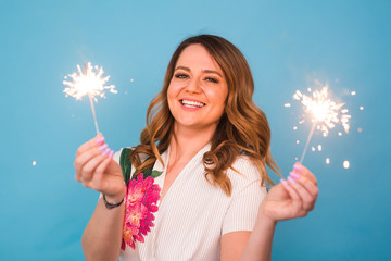 Portrait of a happy woman holding bengal lights over blue background. Christmas, celebrations and...