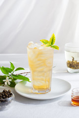 Ice green tea in glass with fresh leaves on white textile background. Copy space