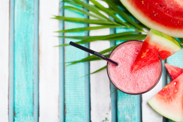 Watermelon smoothie, fresh juice on colorful wooden background with palm leaves. Top view. Copy space